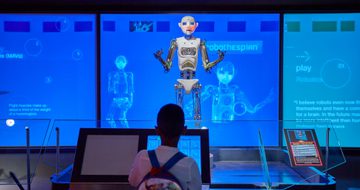 A robot is standing in front of a boy. The robot appears to be talking or singing.