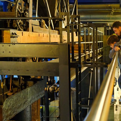 A person and child observe large industrial Smethwick Engine inside a museum.