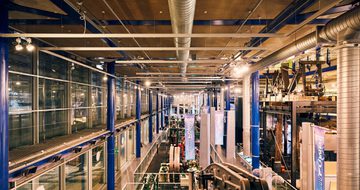 Industrial museum interior with machinery, metal beams, and overhead ventilation ducts.