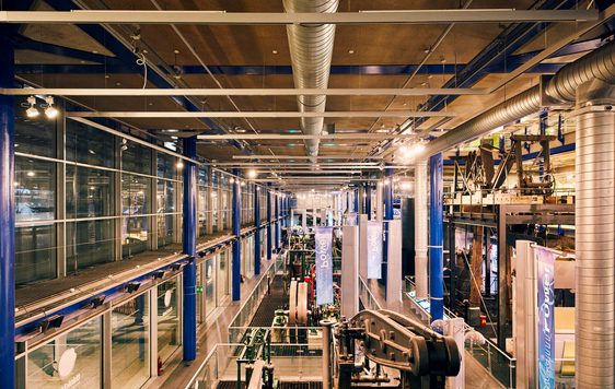 Industrial museum interior with machinery, metal beams, and overhead ventilation ducts.