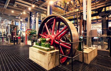 Large industrial machinery with bright red wheels displayed inside a museum setting.