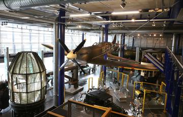 Large exhibition space containing a Spitfire plane suspended over vintage cars and bikes