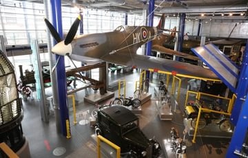 A gallery with planes on display with vehicles below.