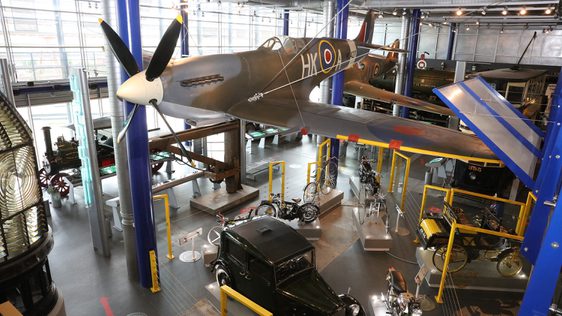 A gallery with planes on display with vehicles below.