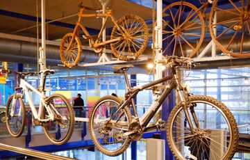 Modern and vintage bicycles displayed over a balcony area in a indoor museum display.