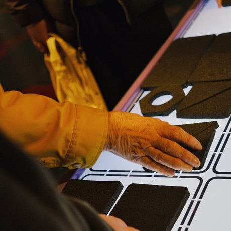 Hands interacting with black cards on a lighted table in a gallery setting.