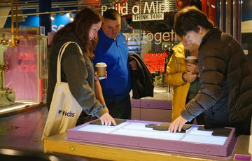 Four people interact with an illuminated tabletop exhibit the gallery.