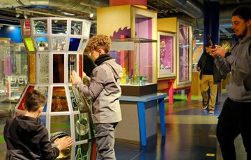 Two children interact with a glazed exhibit while an adult captures the moment on phone.