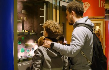 An adult and children observe gemstones displayed behind glass in a museum exhibit.