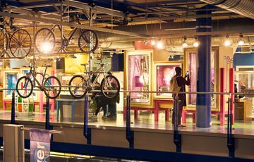 Bicycles displayed in indoor exhibit with a visitors nearby.