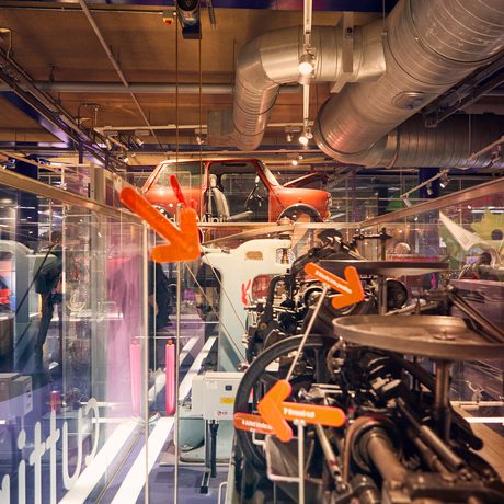 Museum exhibits showcasing a machine with a vintage mini car suspended above in the background.