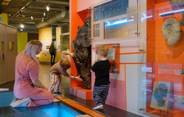 Woman and two children exploring a museum exhibit with fossils and geological displays.