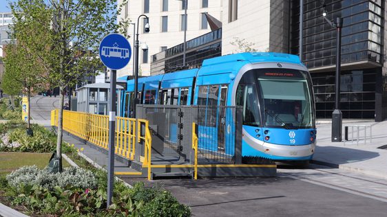 A blue tram alongside a building.