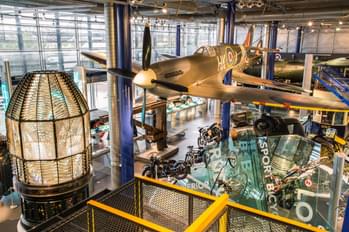 A large gallery space with Spitfire hanging from the ceiling with motorcycles and other vehicles below.
