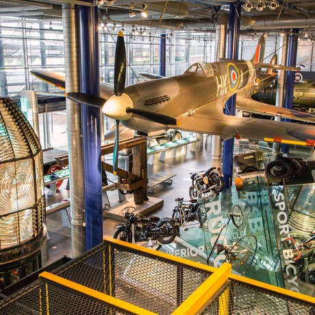 A large gallery space with Spitfire hanging from the ceiling with motorcycles and other vehicles below.