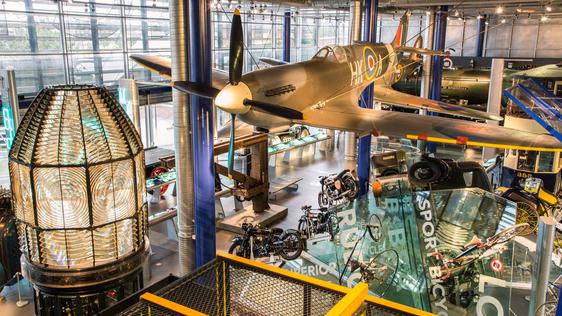 A large gallery space with Spitfire hanging from the ceiling with motorcycles and other vehicles below.