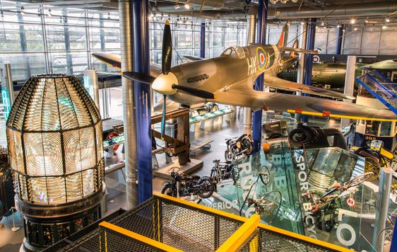 A large gallery space with Spitfire hanging from the ceiling with motorcycles and other vehicles below.