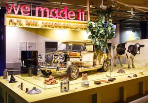 A gallery display featuring a Mini car without panels showing the interior, plus a model cow and tree. A sign above reads 'We Made It'.