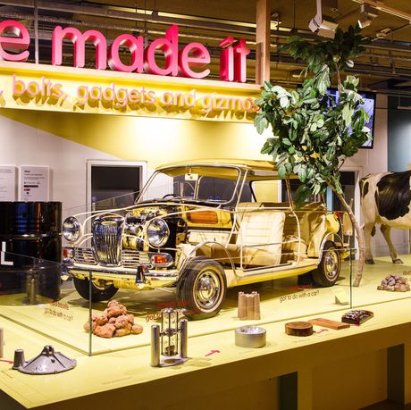 A gallery display featuring a Mini car without panels showing the interior, plus a model cow and tree. A sign above reads 'We Made It'.