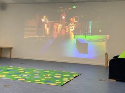 An empty Den space with rug on floor and screen behind with MiniBrum clock tower projected on to the screen.