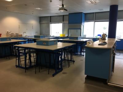 An empty science classroom with stools and tables and equipment around the sides.