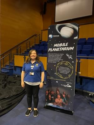 A female learning officer standing next to a sign that reads 'Mobile Planetarium'.