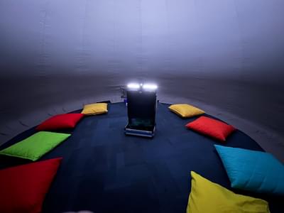 Inside the planetarium with colourful cushions on the floor and projector in centre.