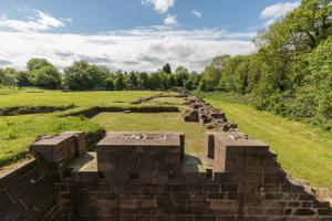 Partial stone walls of a ruined castle in a field surrounded by trees on a bright day