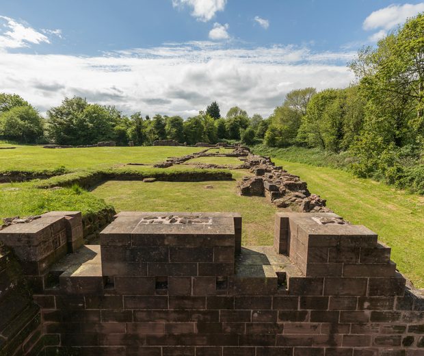 Partial stone walls of a ruined castle in a field surrounded by trees on a bright day