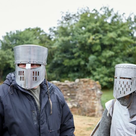 A member of the public wearing a knights helmet, standing by a re-enactor dressed as knight.