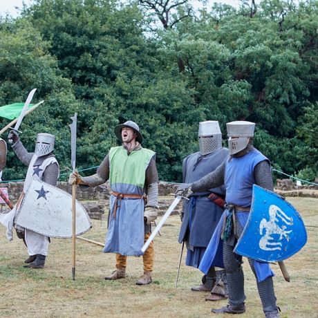 A group of medieval knights, with shields, helmets and flags. They shouting and raising their swords ready for battle.