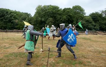 Re-enactors dressed as medieval knights fighting with swords.