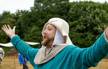 A man dressed in medieval clothes with his arm raised in the air to his side.
