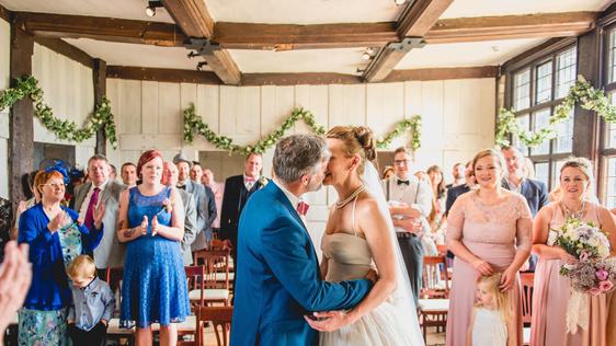 A bride and groom kissing in front of their guests in a Tudor house.
