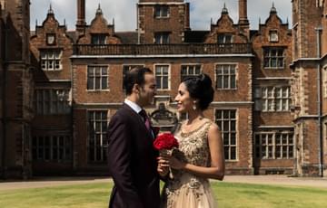 A bride and groom standing outside with Aston Hall in the background