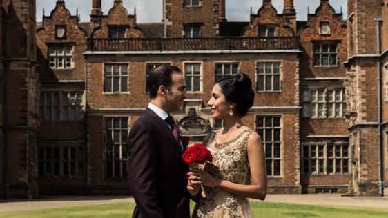 A bride and groom standing outside with Aston Hall in the background