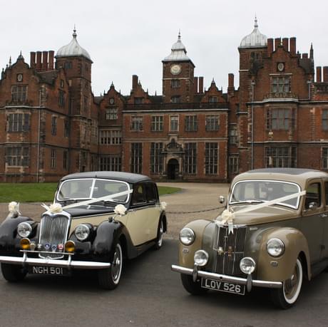 Two vintage cars decorated with ribbon in front of the large historic building of Aston Hall