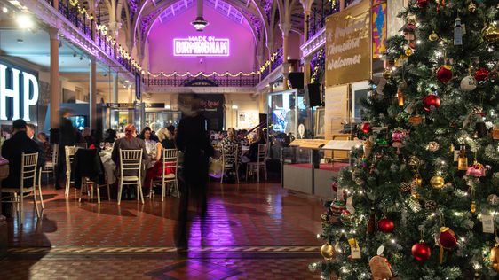 Festive indoor dining with Christmas tree, decorated high ceilings, and neon "Made in Birmingham" sign.