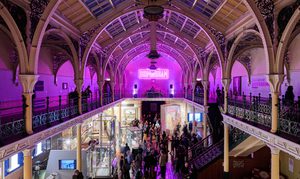 The ornate iron Industrial Gallery at night with visitors inside and lit by the purple neon lights.