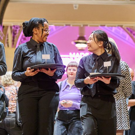 Two waiters looking at each other and holding trays.