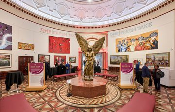People in a the Round Room gallery with large artwork on walls and a winged statue of Lucifer in the centre.