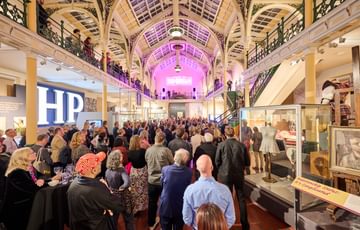 Lots of visitors in two level gallery which has an ironwork ceiling and balcony.