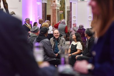 Lots of people in a gallery, in the centre is a group of people sitting and smiling.