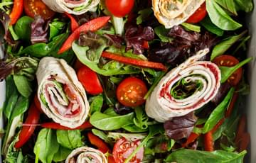 Shot of food from above showing six sliced wraps on a bed of salad leaves with tomatoes and peppers.