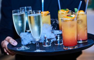 Hands holding tray of drinks. One drink has white smoke coming from it.