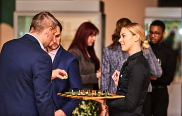 A waitress serving canapés on a tray to two customers.