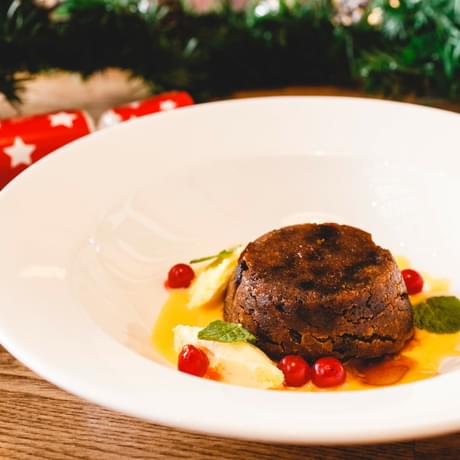 Christmas pudding on a plate with cracker in the background.