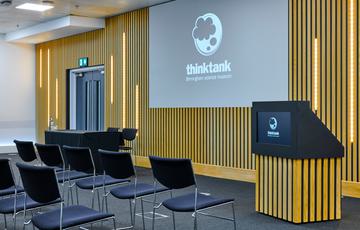 Close up of a room set up in a theatre style seating arrangement with projector and podium.