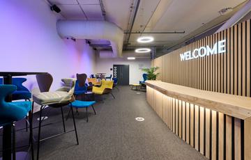 A modern reception area with reception desk, neon 'Welcome' sign and seating areas. The room is lit with purple lighting.