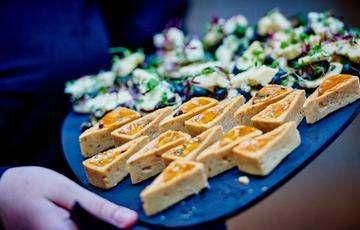 Hands holding a tray of mini pastry triangles and other entrees.